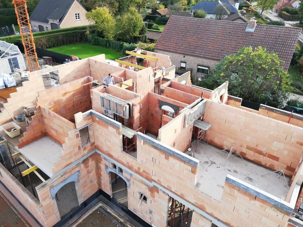 Luchtfoto van een ruwbouwwerf: binnen- en buitenmuren in snelbouwsteen op een betonnen vloerplaat, met torenkraan en stempels
